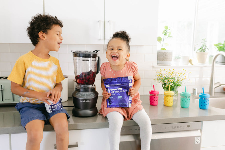 Two kids in the kitchen with a pouch of Growing Up Prebiotics