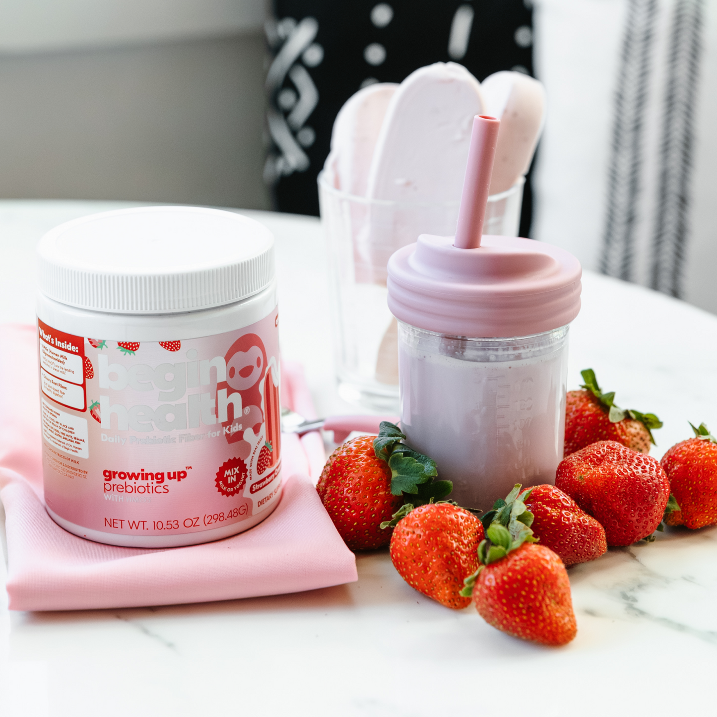 Container of growing up prebiotics with a pink sippy cup and strawberries on a marble surface